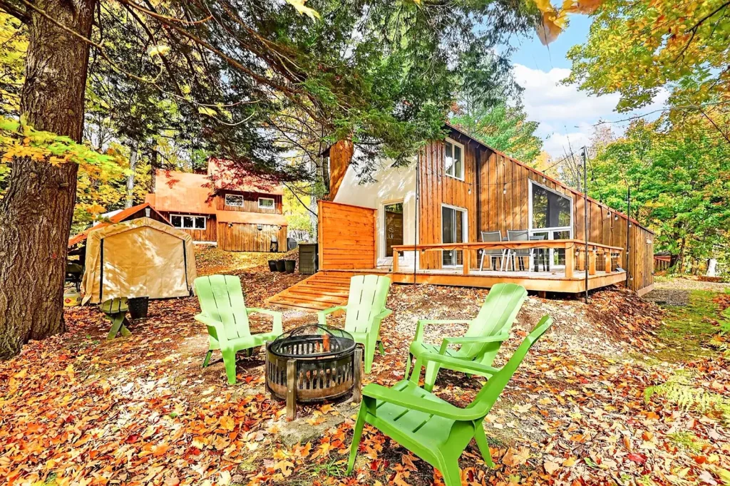 Cour boisée en automne avec chaises Adirondack et foyer extérieur, au 9, rue des Épinettes à Orford